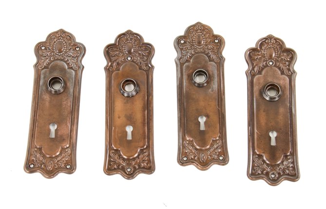 four original early 20th century stamped ornamental wrought steel interior residential doorknob backplates with leafage and cartouche