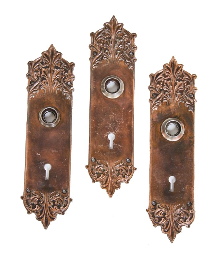 group of three matching early 20th century richardsonian romanesque style copper-plated cast iron "panama" pattern doorknob backplates