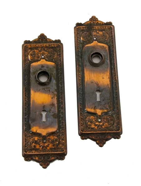 two matching original late 19th or early 20th century "mantua" pattern stamped steel doorknob backplates with oxidized copper-plated finish