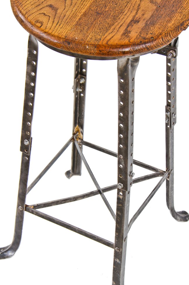 all original and well-maintained fully adjustable c. 1920's antique american industrial four-legged angled steel factory machinist stool with oak wood seat and backrest