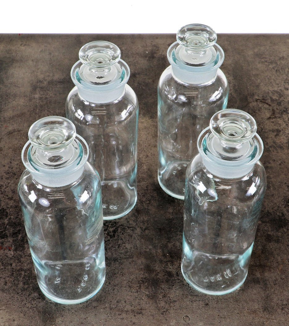 group of four original and intact matching clear glass american industrial research chemistry laboratory reagent bottles with intact circular-shaped tapered ground glass stoppers