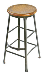 c. 1930's all original shopworn antique american industrial olive green enameled riveted joint angled steel factory stool with intact protruding footrest and solid maple wood seat