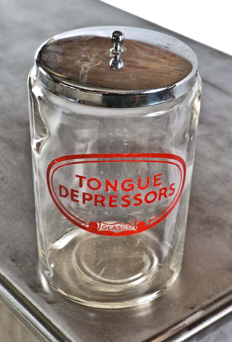 single original and intact antique american oversized medical examination room clear glass cylindrical-shaped jar with baked-on enameled "tongue depressors" oval label