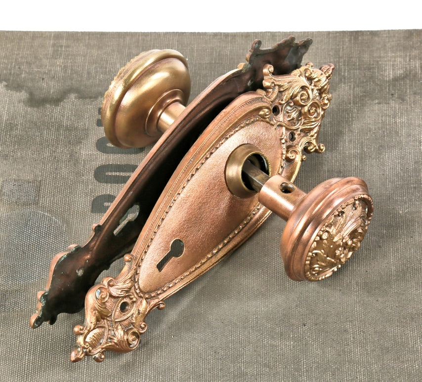 one of several matching brass-plated cast bronze interior residential late victorian era passage door locksets comprised of decorative doorknobs and uniquely shaped backplates