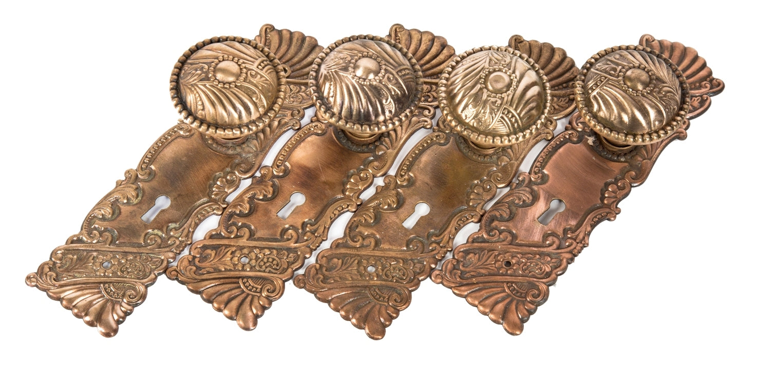 four matching late 19th or early 20th century ornamental wrought brass interior residential passage door backplates and doorknobs in the "roanoke" pattern