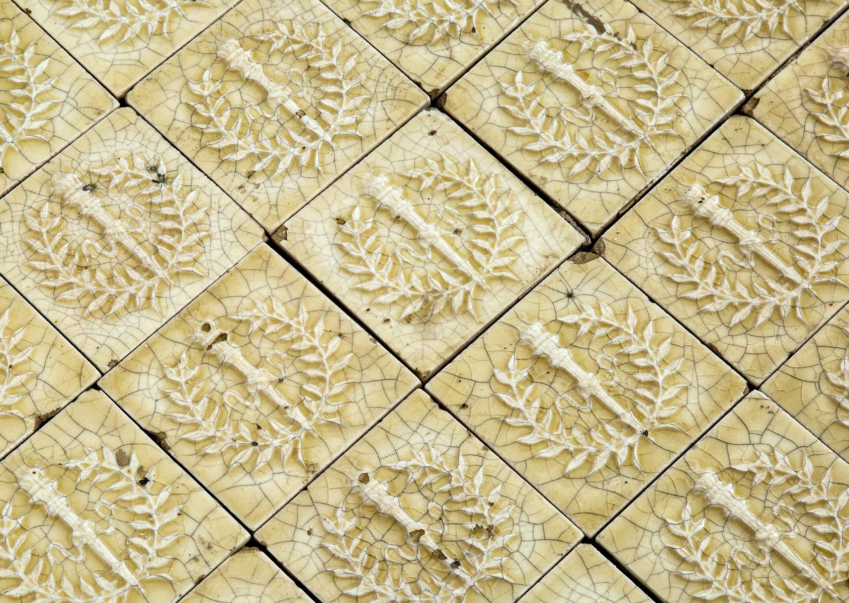 original 19th century 3 x 3 inch yellow glazed deeply embossed majolica tiles with torches and laurel wreaths